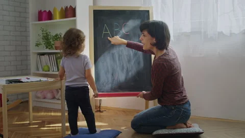Mother teaching child to write letters on chalkboard at home. Stock Footage 252127836