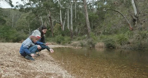 A mother is teaching her young son how to skip stones across a river Video stock 116180367