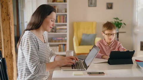 Mother teleworking on laptop while son is distance learning on tablet in Stock Footage 128972220
