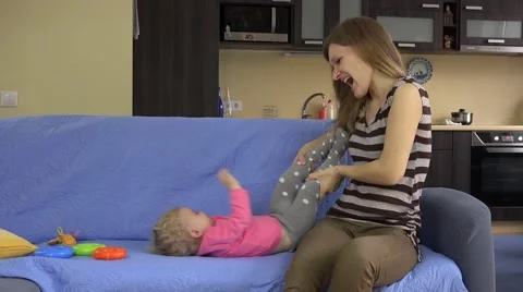Mother tickle and hug baby daughter on blue sofa at home Stock Footage