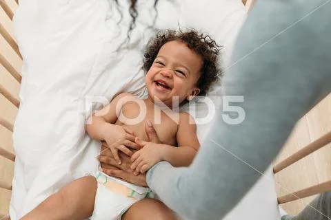 Mother tickling happy baby boy while he lying on crib Stock Photos