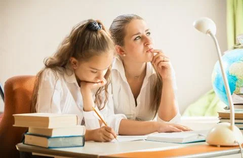 Mother trying to solve complicated exercise with little daughter Stock Photos