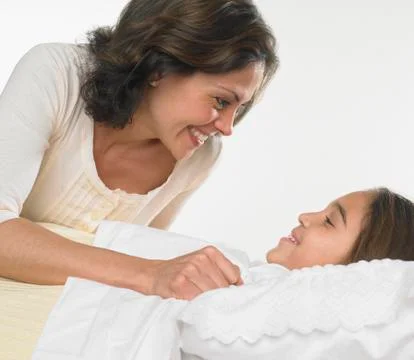 Mother tucking her daughter into bed Stock Photos