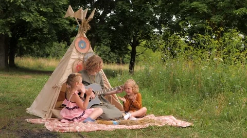 Mother with two cute daughters are playing guitar outdoors Stock Footage 151862976