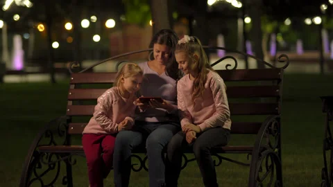 Mother with two daughters looking at a smartphone on a bench in a park - 4k Vídeos de archivo 161186708