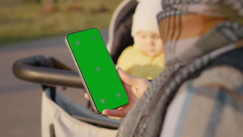 Mother using green screen smartphone next to baby stroller Stock Footage 302465927