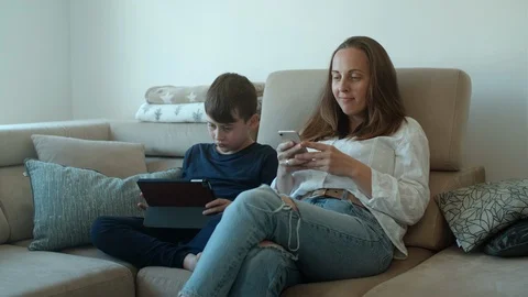Mother  using her phone and her son watching on tablet at home Stock Footage 126986069