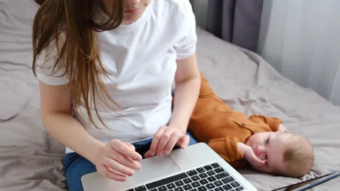 Mother using laptop, sitting on bed near baby daughter at home Stock Footage 151086091