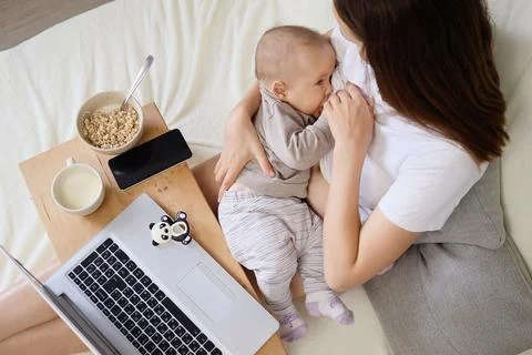 Mother using laptop while breastfeeding baby in the bedroom maintaining con.. Stock Photos