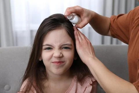 Mother using lice treatment spray on her daughter's hair indoors Stock Photos