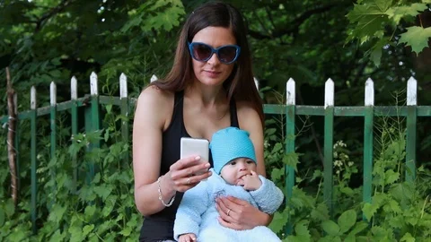 Mother using smartphone while holding her infant baby Stock Footage 124009174