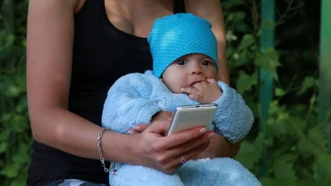 Mother using smartphone while holding her infant baby	 Stock Footage 124009217