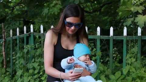 Mother using smartphone while holding her infant baby	 Stock Footage 124009232