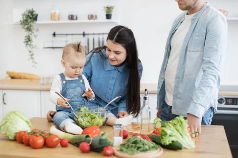Mother using spoons for salad while kid checking greens Stock Photos