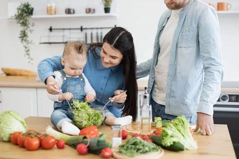Mother using spoons for salad while kid checking greens Stock Photos