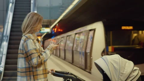Mother waiting for subway train, looking at phone and holding stroller Stock Footage 302473634