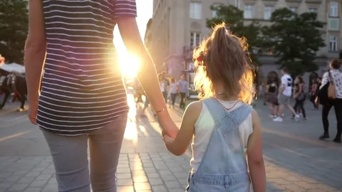 Mother walk with child girl daughter holding her hand in hand in a city in sun Stock Footage
