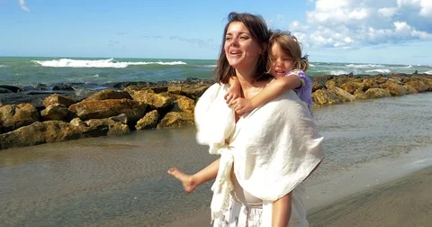 Mother walking on beach holding little daughter on the back singing Stock Footage 82671663