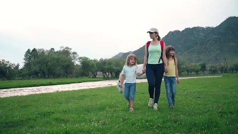 Mother walking with daughters in the meadow with grazing horses. happy family Stock Footage