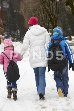 Mother Walking Two Children To School Along Snowy Street In Ski Resort Stock Photos