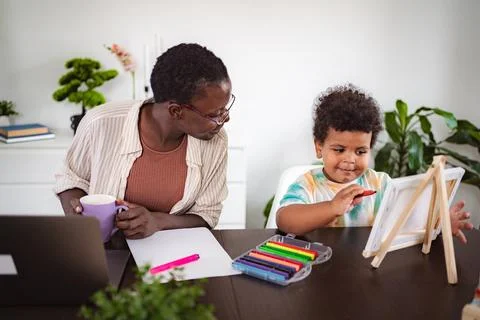 Mother working from home while son drawing on easel Stock Photos