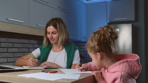 Mother is working in the kitchen at the laptop while her daughter is drawing Stock Footage 148613344