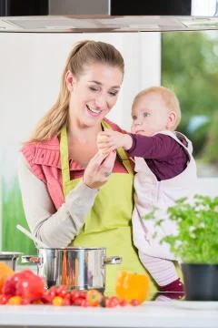 Mother working in kitchen while carrying child Stock Photos