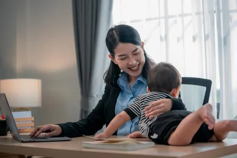 Mother working on laptop while caring for her baby in a bright home office .. Stock Photos