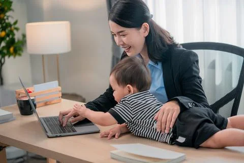 Mother working on a laptop while engaging with her toddler at home office d.. Stock Photos