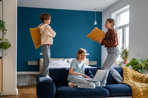 Mother working on laptop while her active noisy children playing with pillows Stock Photos