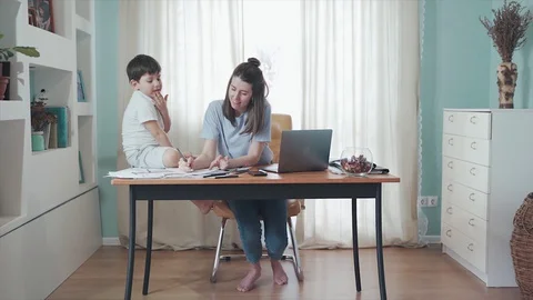 Mother working online from home at the table. A little boy sitting on the table Stock Footage 129381002