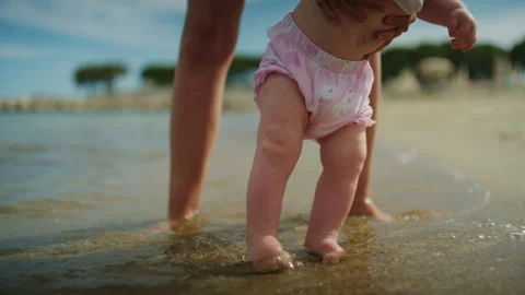 Mother's hands supporting toddler's first steps on a sandy beach, learning to Video stock 339787480