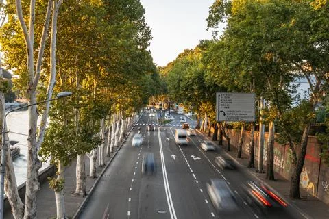 Motion blur traffic on a tree-lined avenue with a river at sunset Stock Photos