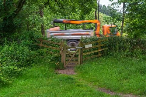 Motion Blurred Construction Vehicle Passing Beside Rural Wooden Gate and Gr.. Stock Photos