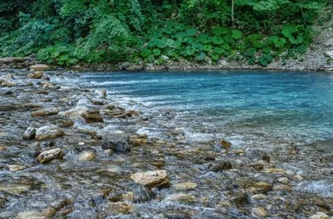 Motion blurred rapids of Khosta River with wet boulders and shore strewn with Stock Photos