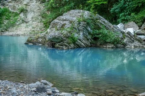 Motion blurred rapids of Khosta River with wet boulders and shore strewn with Stock Photos