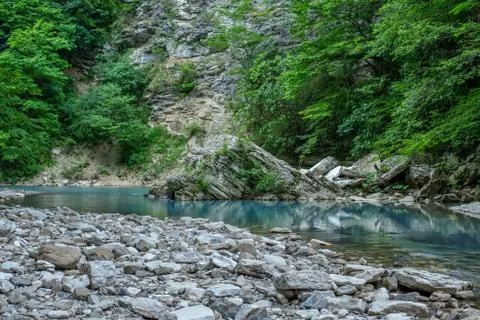 Motion blurred rapids of Khosta River with wet boulders and shore strewn with Stock Photos