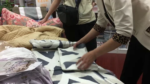 Motion of clerk folding bed sheet for customer inside shopping mall Stock Footage 90361098