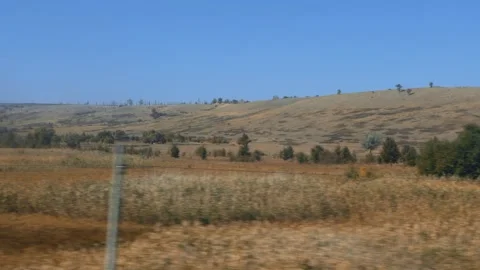 Motion over vast open landscape of dry fields and rolling hills under clear blue Stock Footage 335764173