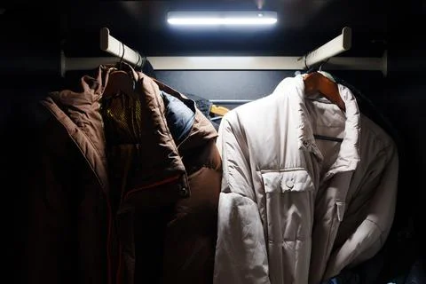 Motion sensor LED lamp illuminates clothes in a dark closet space Stock Photos