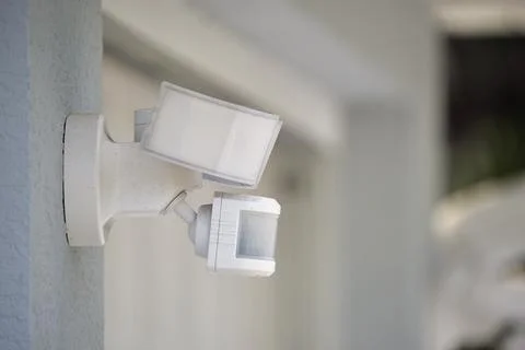 Motion sensor with light detector mounted on exterior wall of private house as Stock Photos