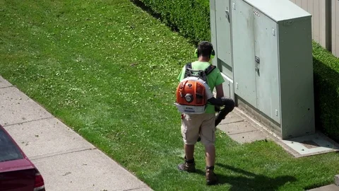 Motion of worker with leaf blowers clean up leaves in front of apartment garden Stock Footage