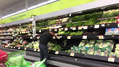 Motion of worker stocking vegetable on display rack inside Walmart store Video stock 275890666