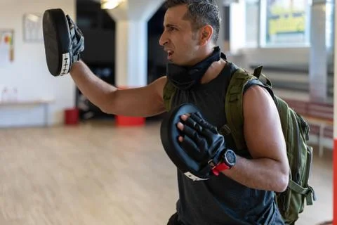 Motivated boot camp instructor stands with punch mitts in gym hall. Portrait Stock Photos