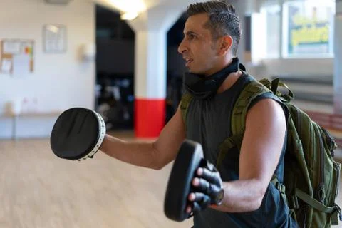 Motivated boot camp instructor stands with punch mitts in gym hall. Training Stock Photos
