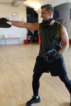 Motivated boot camp instructor stands with punch mitts in gym hall. Training Stock Photos