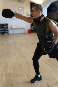 Motivated boot camp instructor stands with punch mitts in gym hall. Training Stock Photos