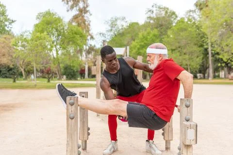 Motivated elderly man exercising on parallel with fit black male instructor Foto stock