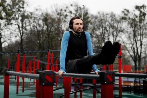 Motivated strongman doing pushups parallel bars in park. Sportsman using local Stock Photos