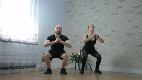 Motivated young couple is training making squats exercises at home in living Stock Footage 128045907